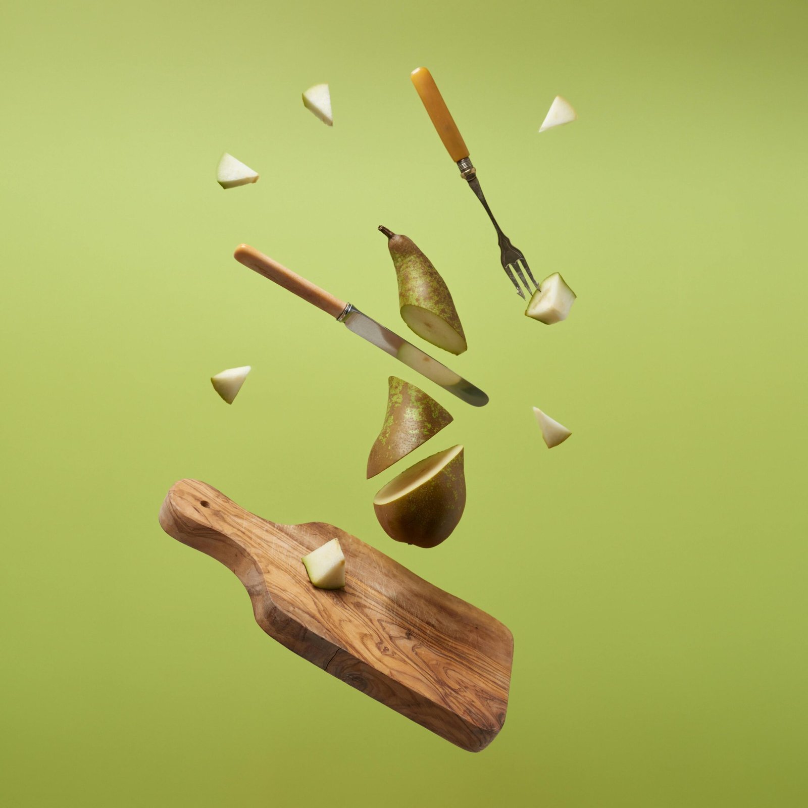 Fresh pear slices with kitchen utensils suspended against a light green backdrop, creating a zero gravity effect.